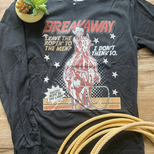 Black t-shirt with graphic design featuring a cowgirl and text, placed on a wooden surface with a coiled rope and plant.